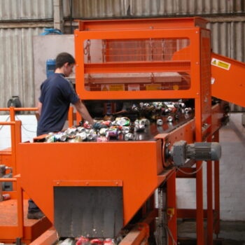 Image of workers hand-sorting materials at a can separation plant, with magnetic separation equipment visible in the background.