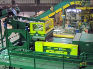Drum magnet receiving dry recyclables from a vibratory feeder, removing ferrous metals before non‑ferrous separation on the eddy current separator.