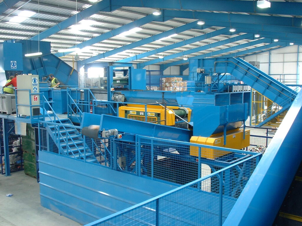 Image of a Material Recovery Facility (MRF) in operation, featuring conveyor systems and magnetic separation equipment sorting recyclable materials. data-large-image=