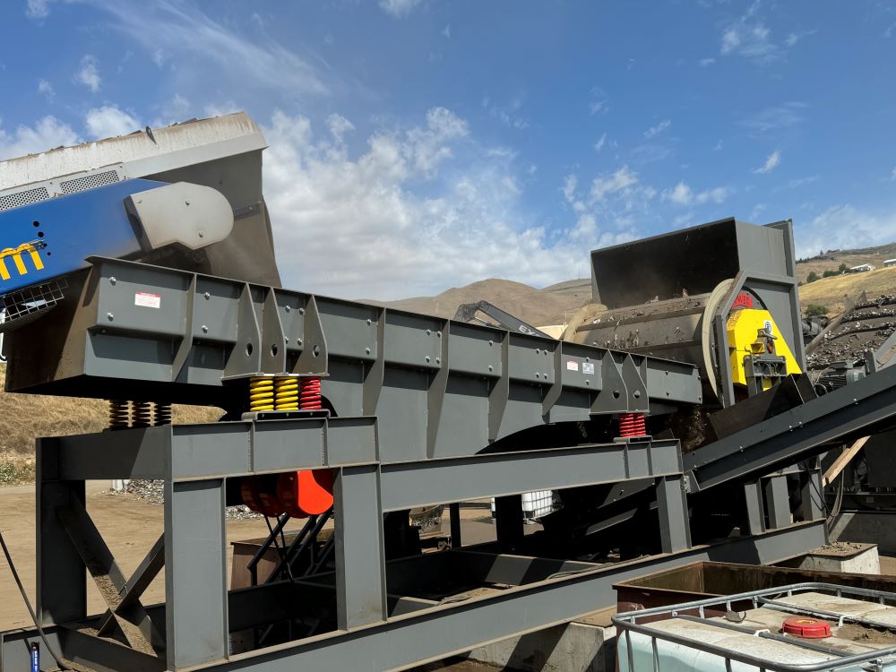 Industrial vibratory feeder regulating material flow on a recycling processing line. data-large-image=